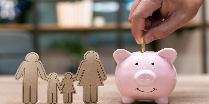 a hand holding a small pink piggy bank with a note