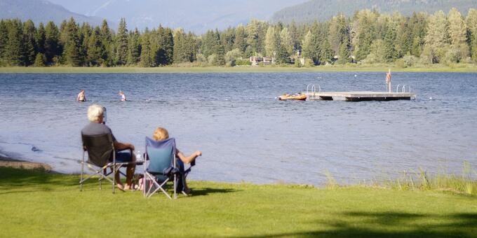 a group of people sitting in chairs on a grassy field by a lake