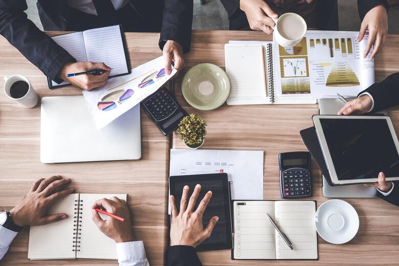 a group of people sitting at a table with papers and pens